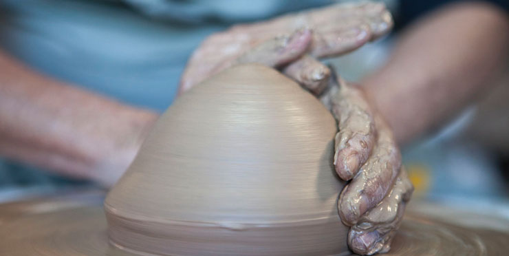 A artista com a mão na massa, fazendo o molde de um pote no torno